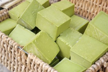 Woven basket holds several green soap bars at an outdoor market.