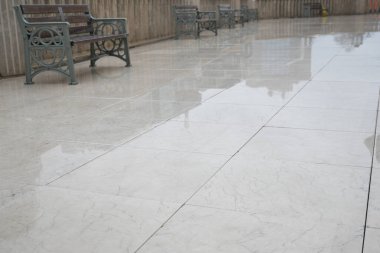 Marble flooring shines in a city plaza with benches after rainfall.