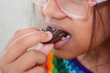 Gözlüklü genç kız çikolatalı kurabiyeyi ısırıyor, atıştırmanın tadını çıkarıyor..