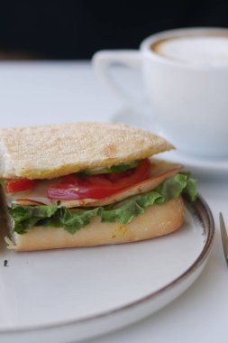 Turkey sandwich with lettuce and tomato, beside a cup of coffee.