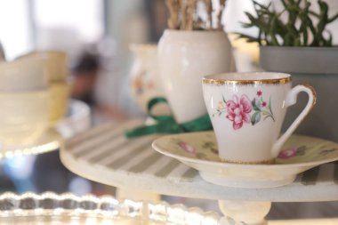 A delicate teacup and saucer sit on a wooden shelf in a cozy environment.