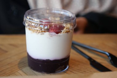 Yoğurt, meyve ve granola katmanlı bir tatlı ahşap bir masada oturur..