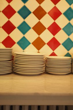 A stack of white plates stands against a bright, patterned wall.