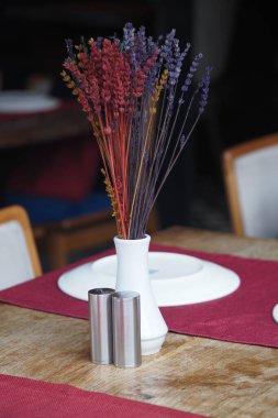 A simple table setting featuring a vase of dried flowers and salt shakers.