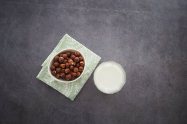 Hazelnuts are arranged in a bowl next to fresh milk on a table.