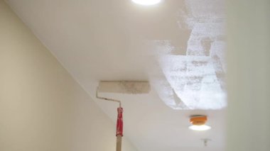 Bir insan, iyi aydınlatılmış bir koridorun tavanını tekerlekli fırçayla boyuyor..