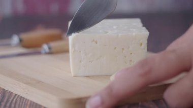 Birisi mutfak masasında bir kalıp taze peyniri bıçakla dilimliyor..