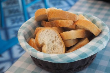 Hasır sepette damalı masa örtüsünün üzerinde taze ekmek dilimleri var..