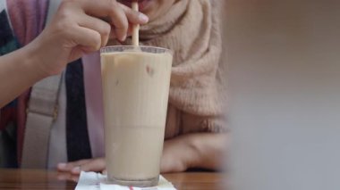 Bir insan sıcak, davetkar bir kafede buzlu bir içecek yudumlar..