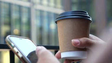 İnsan kahve içer ve şehir ortamında telefona bakar..