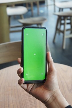 Bir kafede yeşil ekran gösteren bir akıllı telefon tutan bir kişi var..