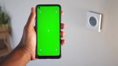 Parlak bir odada yeşil ekranlı akıllı telefonu tutan bir el..