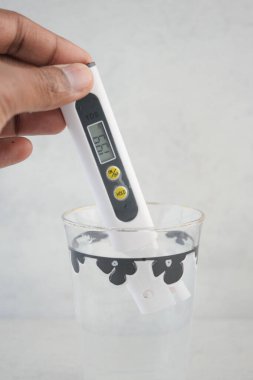Bir el, temiz bir bardak suyun içinde dijital termometreyi tutar..