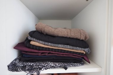 Birkaç katlanmış giysi düzgünce bir rafa dizilmiştir..