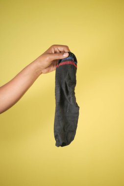 Bir insan sarı arka planda kirli siyah bir çorap tutar..