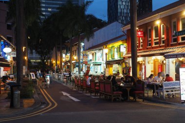 Ziyaretçiler gece boyunca hareketli bir cadde boyunca yiyecek ve içeceklerin tadını çıkarıyorlar..