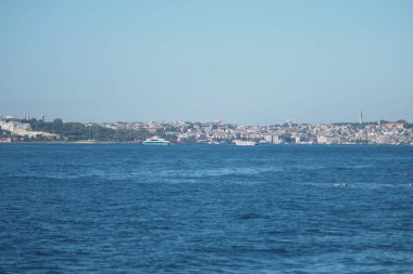 Parlak bir gökyüzünün altında sakin sularda kayıkları olan canlı bir sahil şehri..