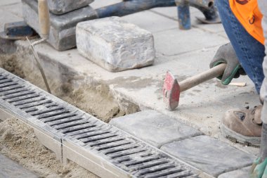 Bir inşaat işçisi kaldırıma taş koymak için çekiç kullanıyor..