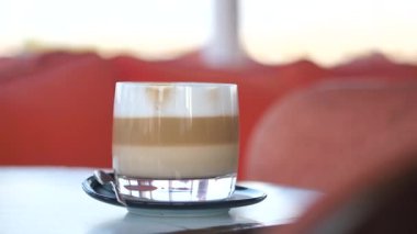 Sıcak bir kafe atmosferindeki masada kremalı bir latte duruyor..