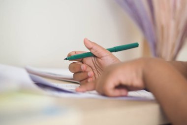 Genç bir çocuk çalışma masasında çalışırken yeşil bir kalem tutuyor..