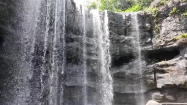 Yeşillik tarafından çerçevelenmiş kayaların üzerinde çağlayan bir şelale hissedin..