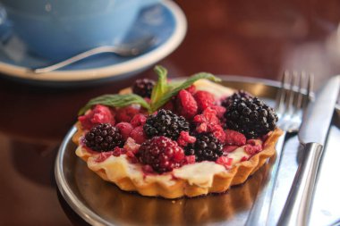 İçinde ahududu ve böğürtlen bulunan bir turta gümüş bir tabakta duruyor..