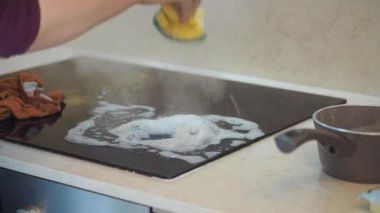 Buhar yükselirken bir kişi sobayı temizlemek için sabun ve sünger kullanır..