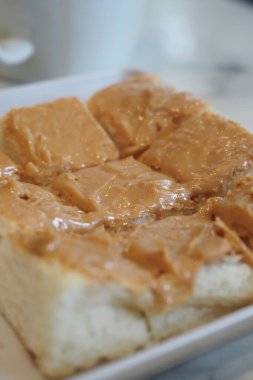 Yumuşak fıstık ezmesiyle kaplı kalın bir dilim ekmek bir tabakta oturur..