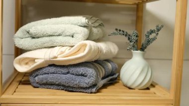 Yumuşak havlular ahşap bir rafta küçük bir vazoyla düzgünce dizilir..