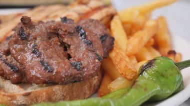 Kızarmış patates ve taze yeşil biberle servis edilen sulu ızgara et..