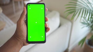 Kullanıcı, şık bir oturma odasında yeşil ekranlı akıllı telefon gösteriyor.