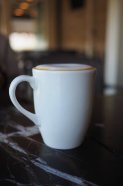 Kahve dolu beyaz bir kupa bir kafede mermer bir masada oturuyor..