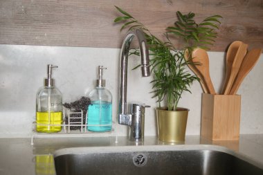 Temiz mutfak lavabosunda sabun makineleri, küçük bir bitki ve çatal bıçaklar var..