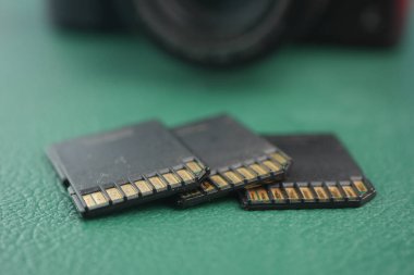 Üç siyah hafıza kartı bir kameranın yanındaki yeşil bir yüzeyde duruyor..