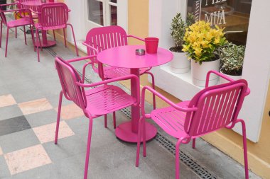 Renkli pembe sandalyeler ve canlı bir kafe ortamında yuvarlak bir masa..