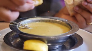 Bir insan yerel bir lokantada lezzetli bir çorba kâsesine ekmek batırır..