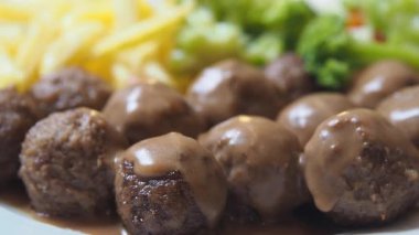 Yanında taze sebze ve sosla kaplı bir tabak köftenin tadını çıkar..