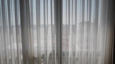 Perdelerin arasından ışık parlıyor. Dışarıdaki canlı şehir manzarasını ortaya çıkarıyor..