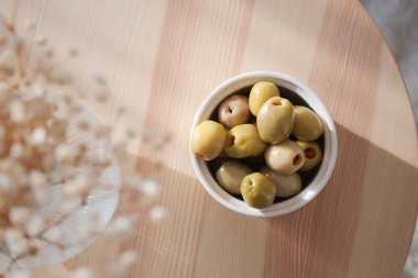 Yeşil ve kahverengi zeytinlerle dolu bir kase gün ışığında ahşap bir yüzeyde oturur..