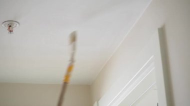 Bir insan uzun bir fırça kullanarak parlak bir odanın tavanını boyar..