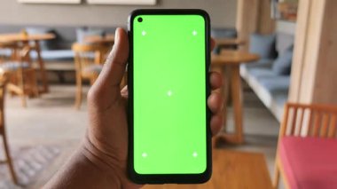 Sade yeşil ekranı olan akıllı bir telefon gösteren bir kişi..