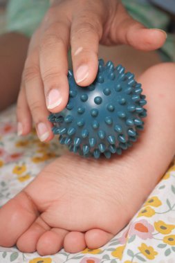 Rahatlamak ve rahatlamak için çocuk ayağına dikenli bir masaj topu sarar..