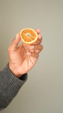 Bir el, tarafsız bir arkaplanda kurumuş portakal dilimini gösterir..