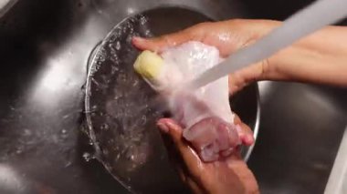 Evdeki mutfak lavabosunda taze tavuk temizliyorum.,