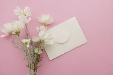 Pembe bir yüzeydeki basit bir zarfın yanında taze beyaz çiçekler..