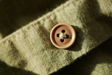 Bir düğme dokulu yeşil kumaşa dayanır, gelişigüzel biçim ve ayrıntıları vurgular.