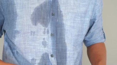 Bir adam egzersizden sonra mavi gömleğinde belirgin ter lekeleri gösterir..