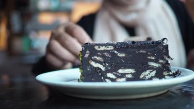 Bir insan sıcak bir kafede bir tabakta bir dilim çikolatalı pastaya uzanır..