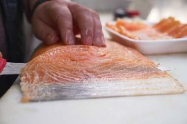 Bir şef, temiz bir tezgahta taze somon filetosunu ustalıkla dilimler..