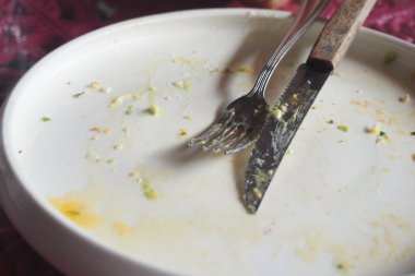 Çatal ve bıçak boş bir tabakta dinleniyor. Yiyecek kalıntılarını gösteriyor..